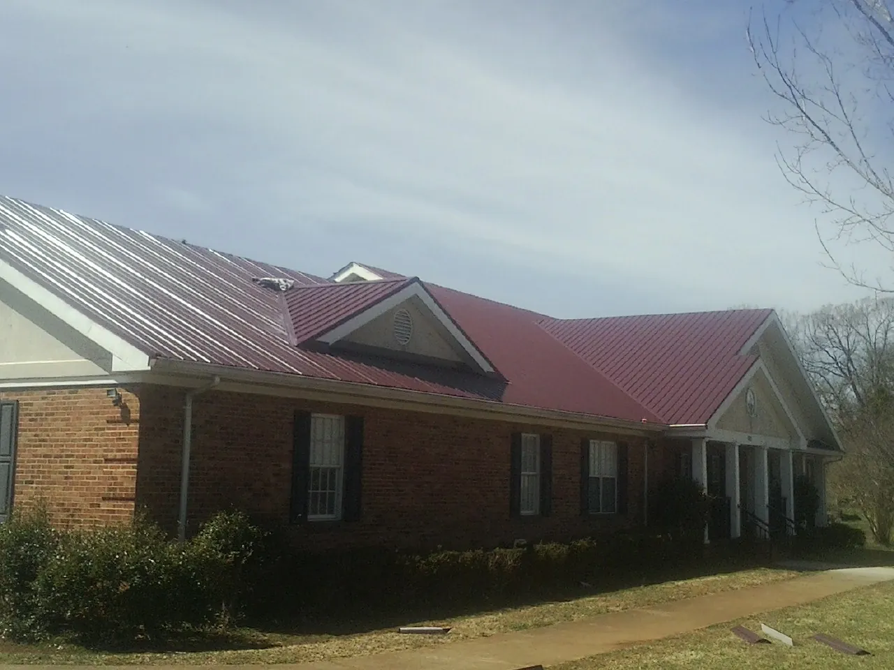 Red metal roof with gabled entries on a long brick building, from a Hail Damage Roof Repair job in North Little Rock