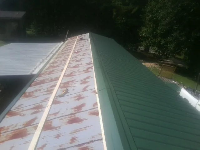 Old rusted panels beside newly installed green metal roofing — Wind Damage Roof Repair by Roofing Brothers in North Little Rock
