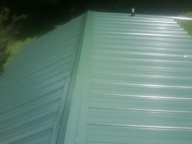 New green metal panels meeting at the ridge of a roof — Flat Roof Repair work by our crew in North Little Rock