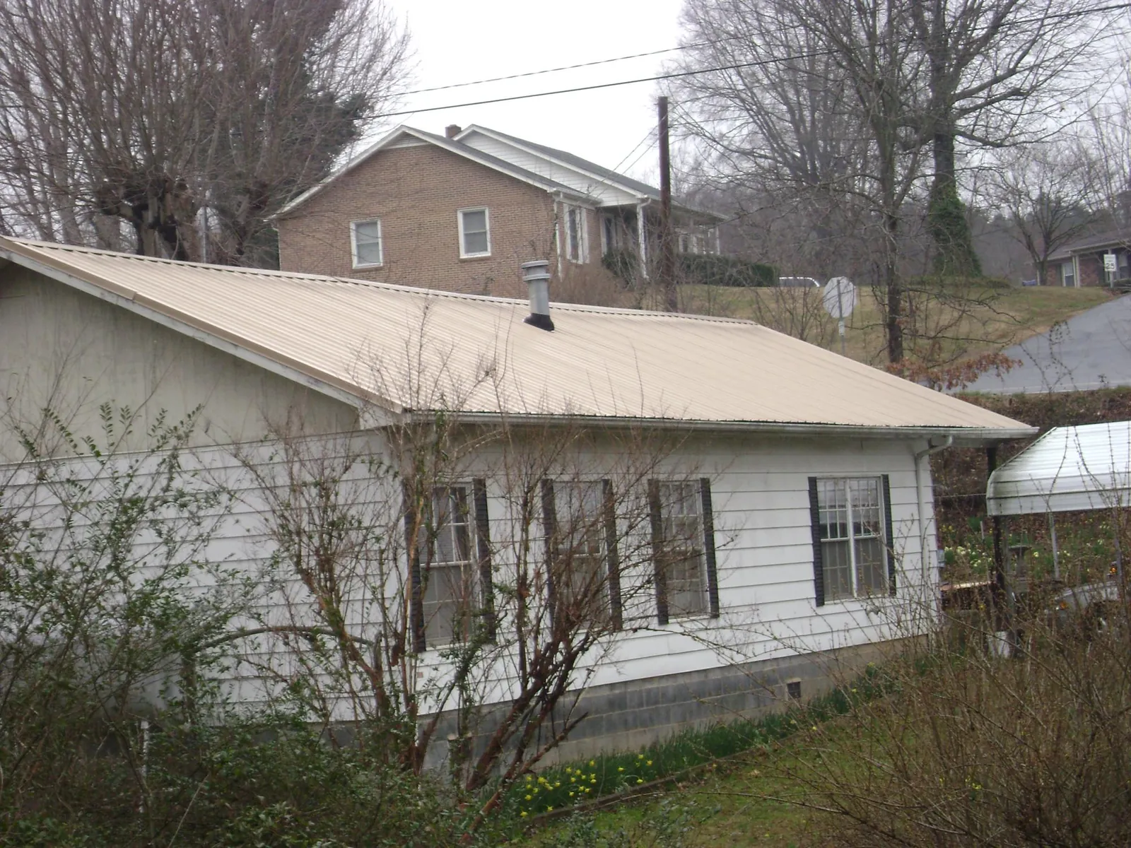 Tan metal roof on a white sided house set into a hillside — Commercial Roofing by Roofing Brothers in North Little Rock
